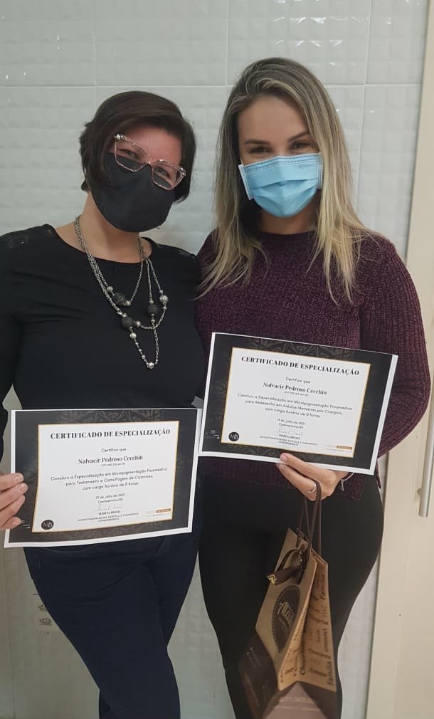 Duas alunas de máscara com seus certificados de especialização